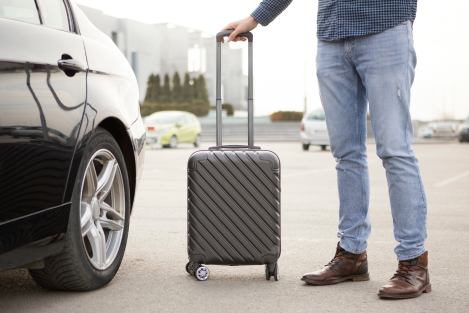 man standing beside rental car with suitcase